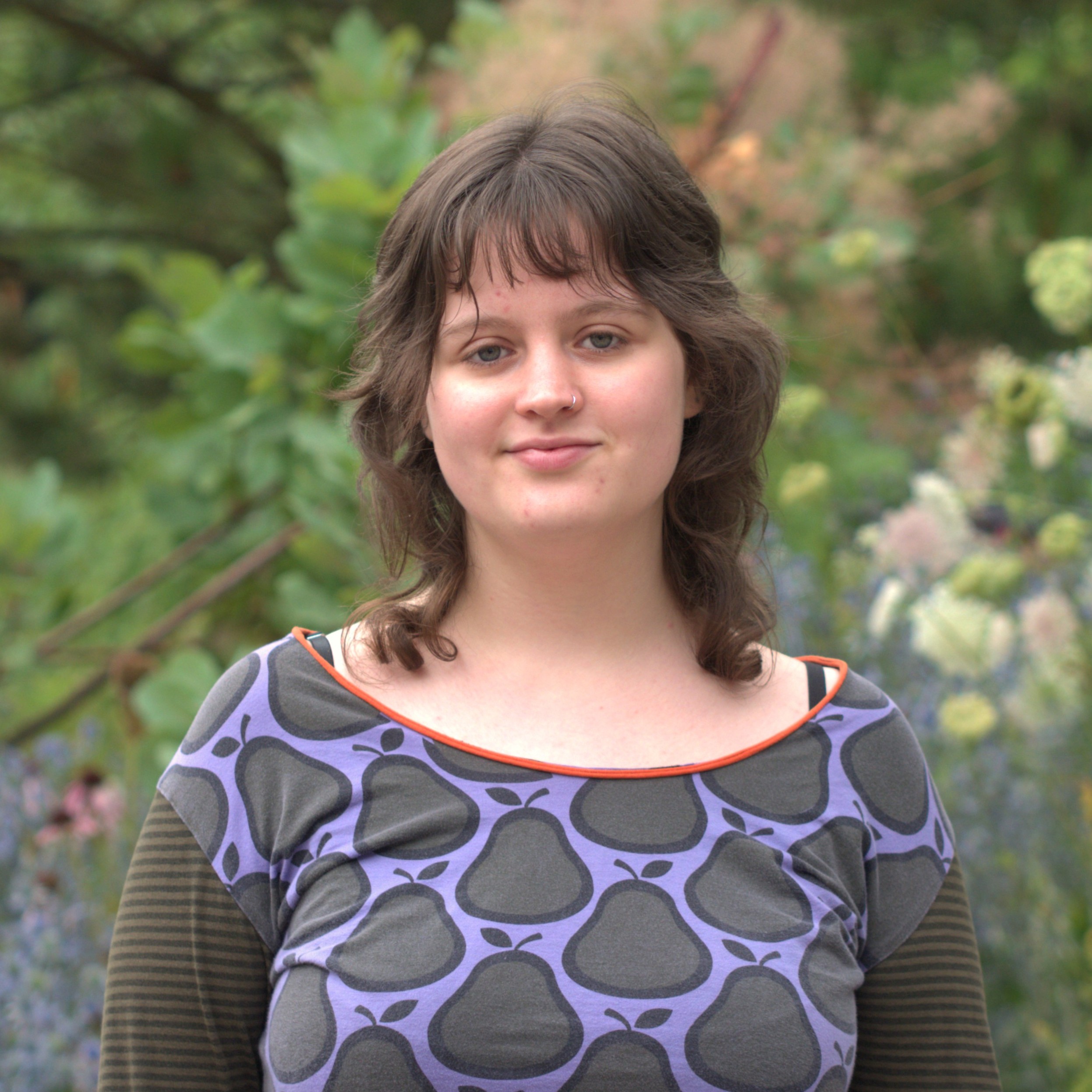 Portrait photo of Mia von Hadel: A dark-haired young woman against the backdrop of a garden landscape.