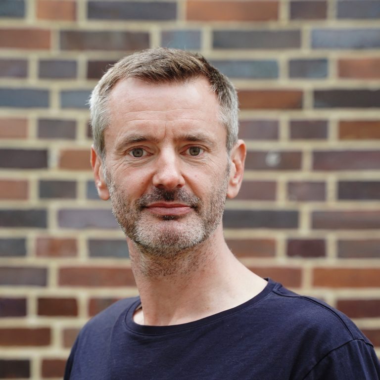 Portrait photo of Dr. Immo Graf: A slender man with gray hair and a short gray beard, wearing a dark blue shirt.