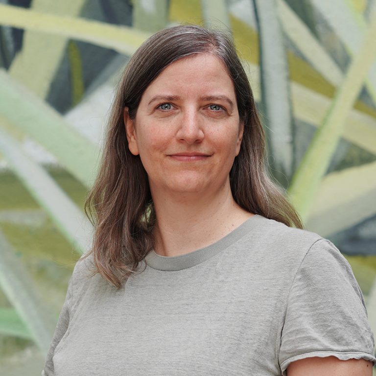 Porträtfoto von Tatjana Thiel: Eine grauhaarige Frau mittleren Alters mit grauen Augen, die ein hellgrünes T-shirt trägt.