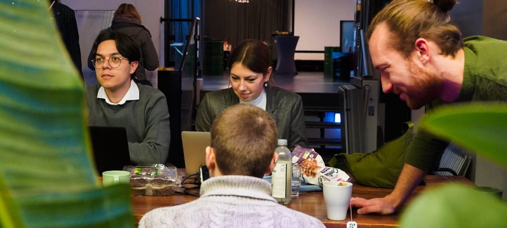 Vier junge Leute arbeiten gemeinsam an einem Tisch zwischen grünen Zimmerpflanzen.