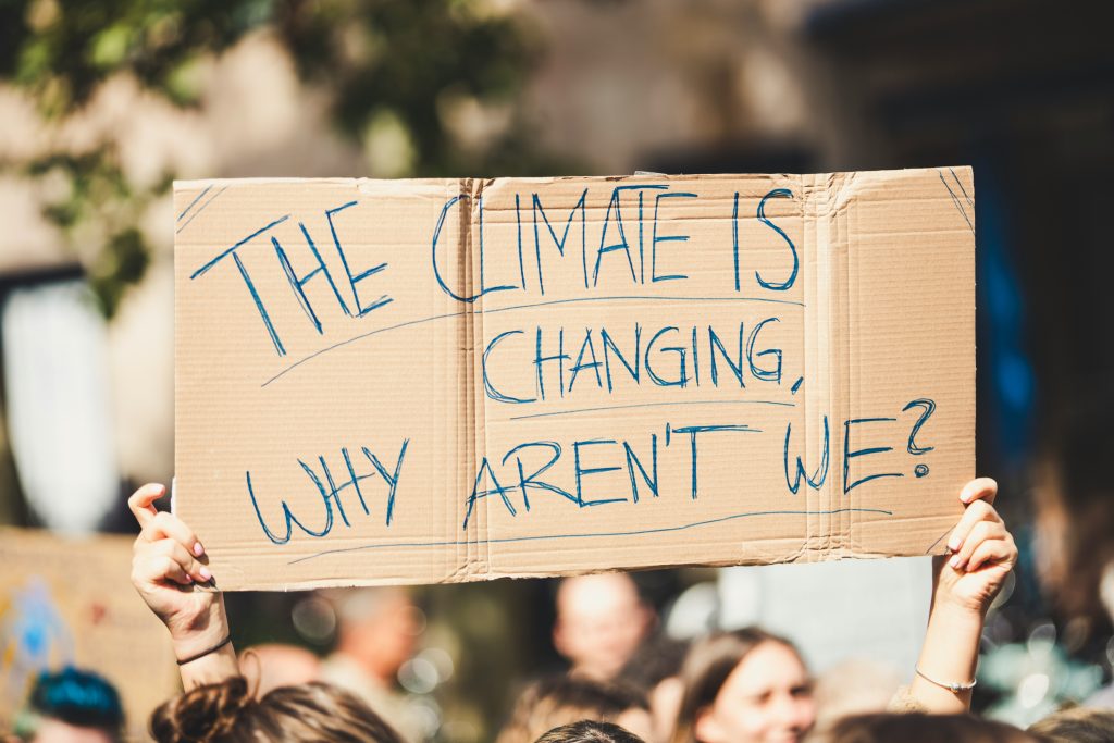Eine Person hält ein Pappschild hoch mit der Aufschrift "The Climate is changing, why aren't we?"