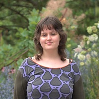 Portrait photo of Mia von Hadel: A young woman with dark hair against the backdrop of a garden landscape.