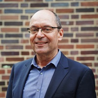 Portrait photo of Marcel Keiffenheim: A smiling man with gray hair, a receding hairline, and glasses, wearing a dark blue suit jacket and a light blue shirt.