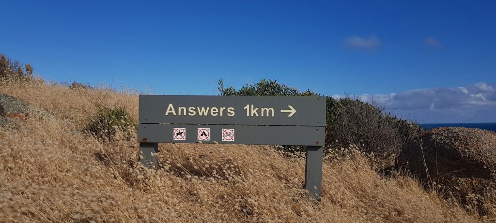 Schild an einem Hügel mit der Aufschrift "Answers 1km" gefolgt von einem Pfeil nach rechts. Im Hintergrund sind trockenes Gras und blauer Himmel zu sehen. Bildcredits: Foto von Hadija auf Unsplash.